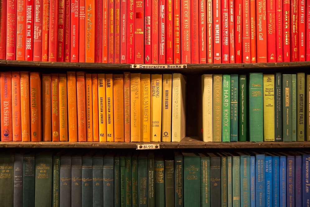 Des livres de la même hauteur classés par couleurs dans une bibliothèque à plusieurs étages