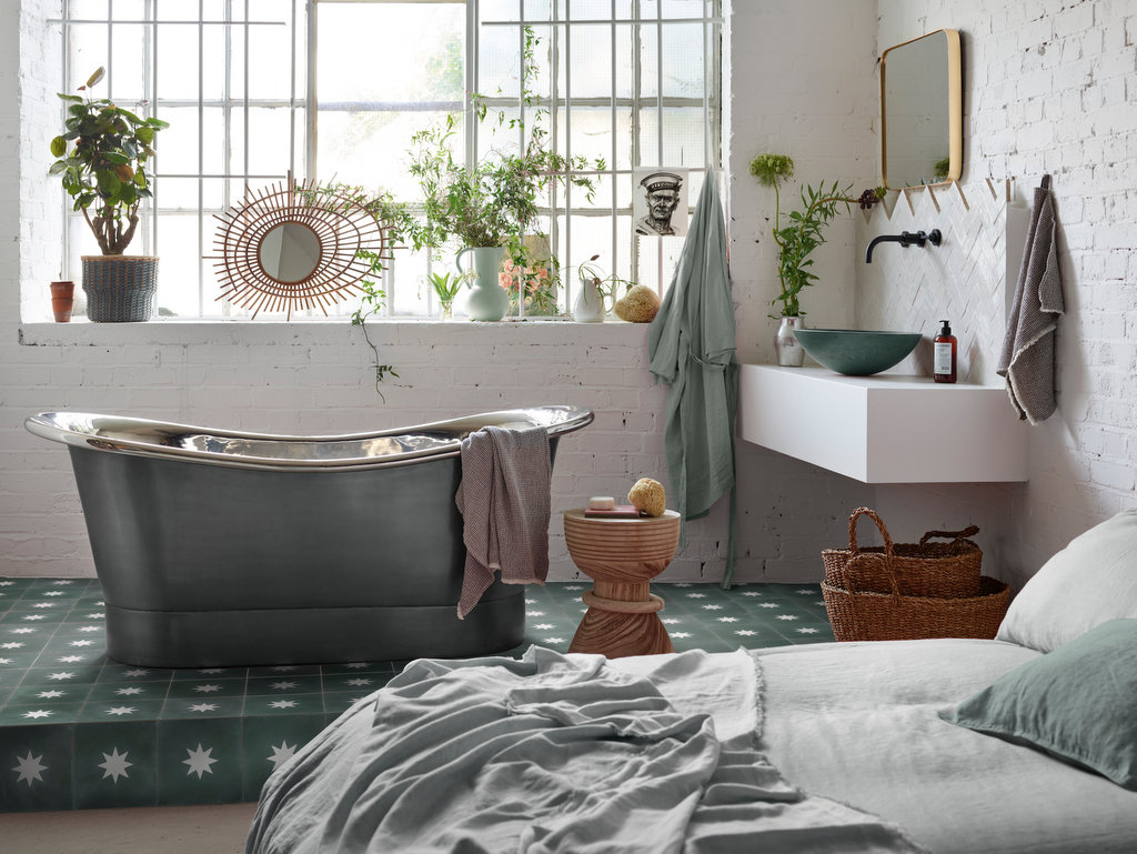 La baignoire se trouve juste à côté du lit, sur un sol adapté : baignoire de style rétro et carreaux de ciment au sol