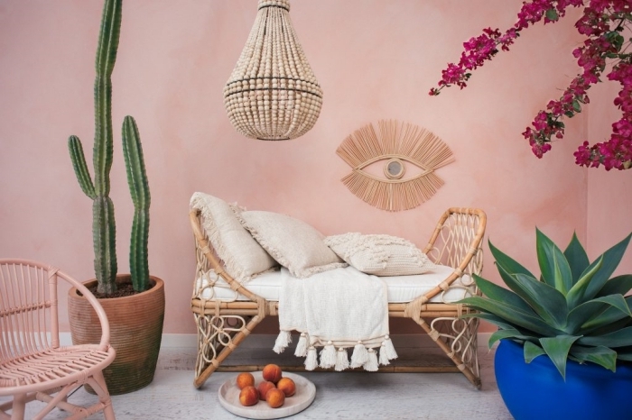 Un meuble en rotin dans cette pièce à la déco exotique, avec un mur ocre clair, un cactus et un bougainvilliers