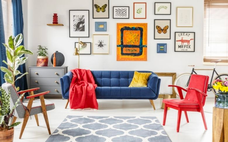 Une pièce de vie arty aux couleurs du printemps, avec un canapé bleu, un fauteuil rouge, un coussin jaune et des tableaux papillons au mur