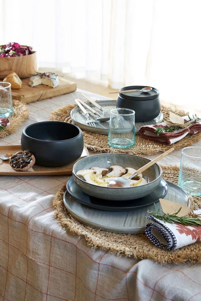 La vaisselle est en terre cuite ou en grès, tandis que la nappe est en coton et les sets de table en raphia
