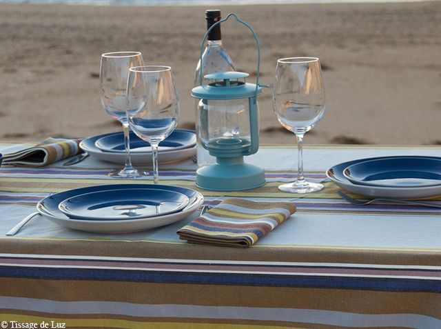 Installée sur la plage, la table est recouverte d'une nappe tissu bayadère, avec des assiettes bleues