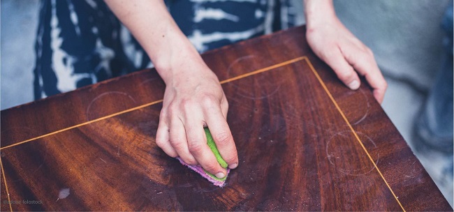 Rénover un meuble en bois en nettoyant bien sa surface vernie à l'aide d'une éponge