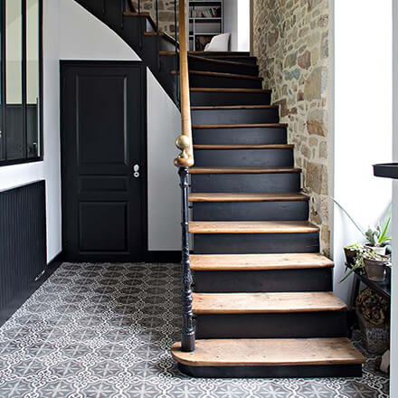 Cette cage d'escalier authentique s'orne d'un mur en vraies pierres, et de marches en noir et bois, tandis que le sol est en carreaux de ciment