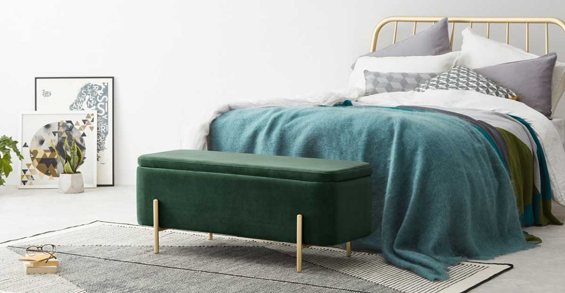 Un coffre banc assise de couleur verte au pied du lit