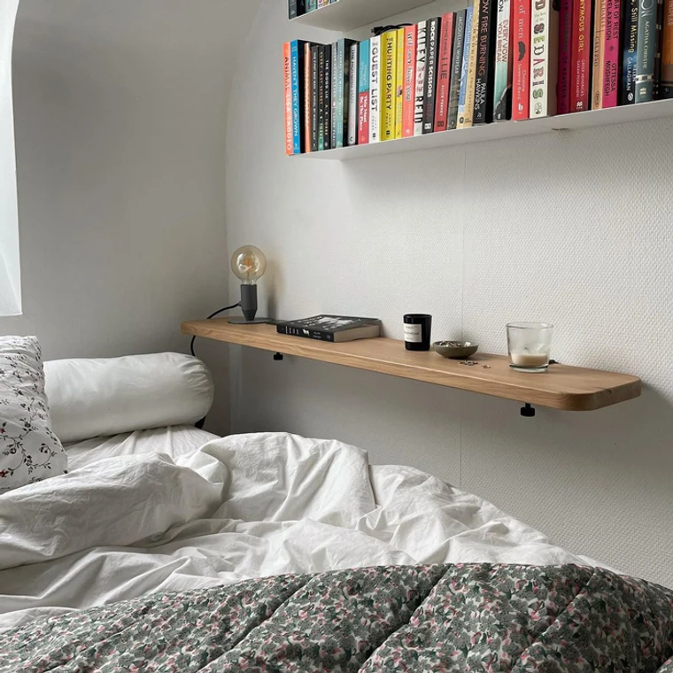 Une étagère constituée d'une planche en bois, au-dessus du lit