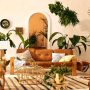 Un grand salon lumineux qui se pare d'une belle déco coloniale, avec un tapis artisanal, des meubles en bois et de nombreuses plantes vertes