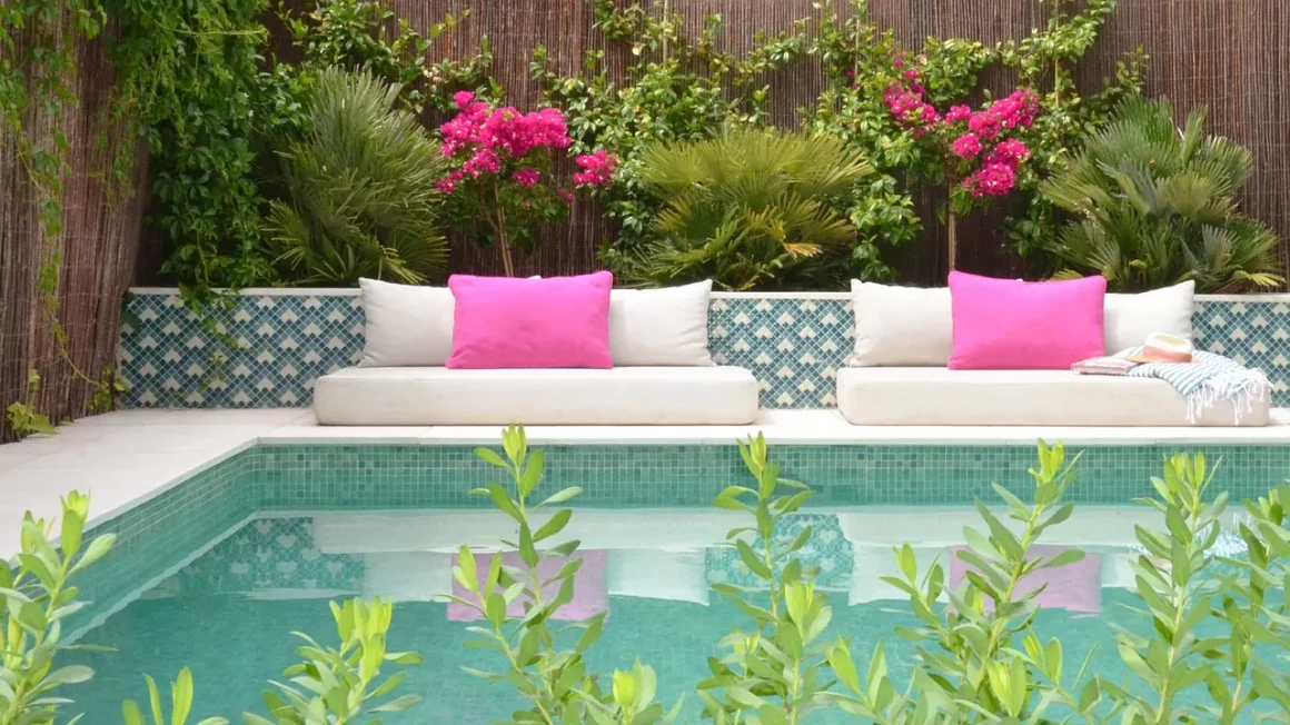Une grande terrasse de piscine avec des coussins colorés, assortis au rose vif des bougainvilliers derrière