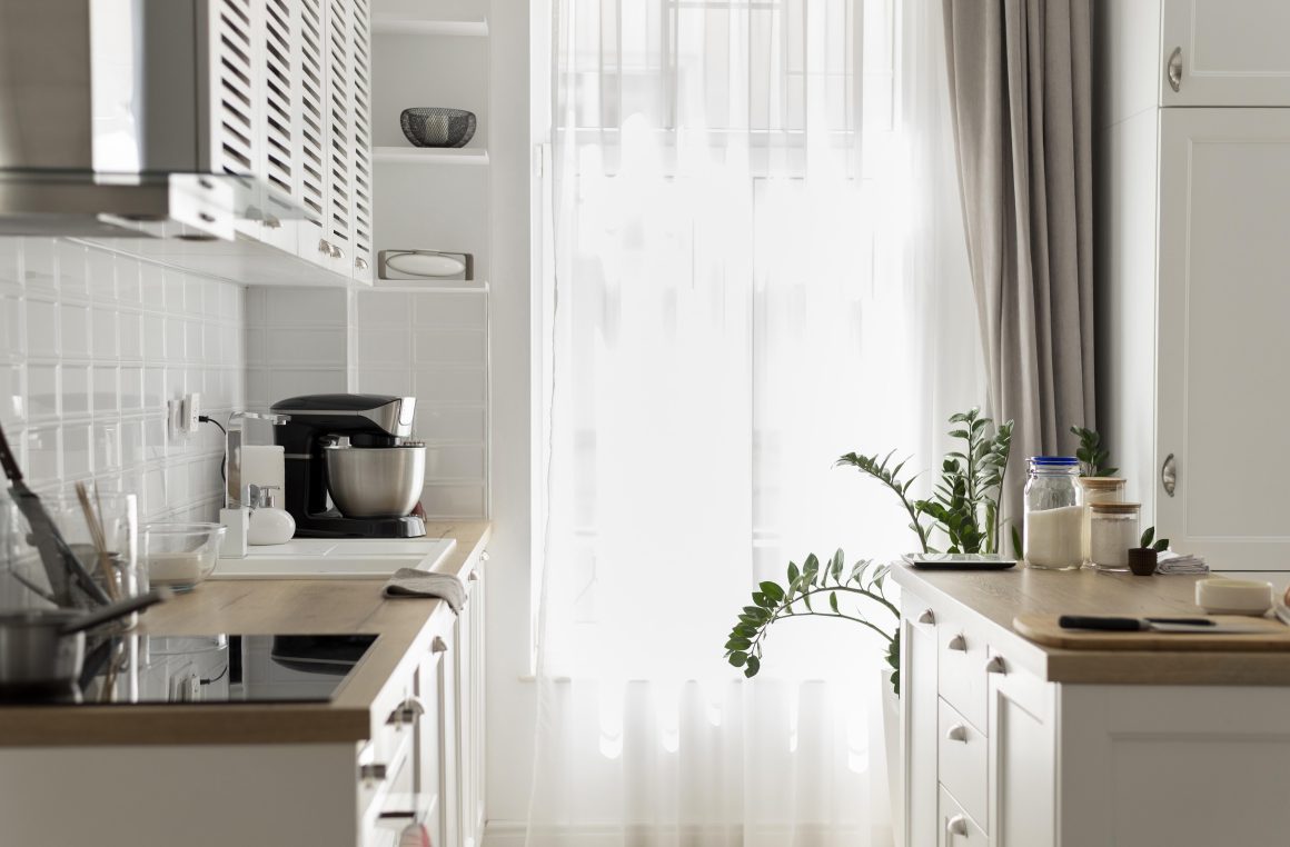 ambiance printanière dans une cuisine blanche et lumineuse avec des rideaux légers et de la verdure