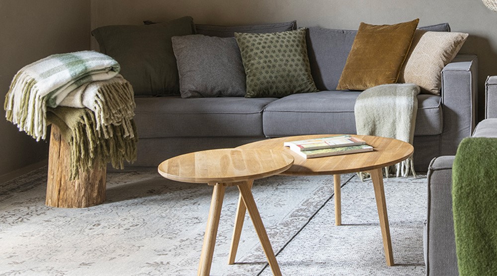 table basse ronde style scandinave dans un salon avec déco cosy, un canapé en gris, des plaids et deux tapis