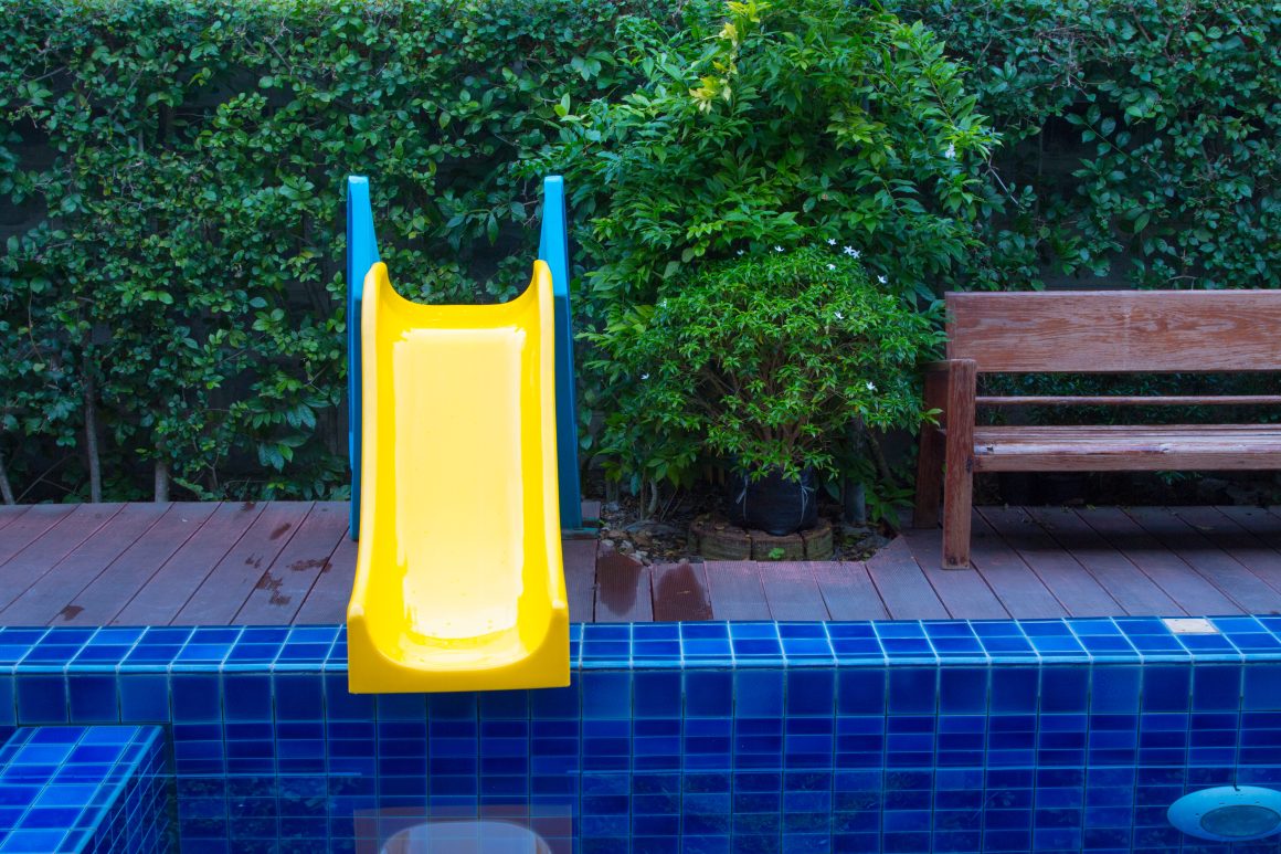 Déco piscine zen avec un petit toboggan jaune et bleu, entourée de végétation dense