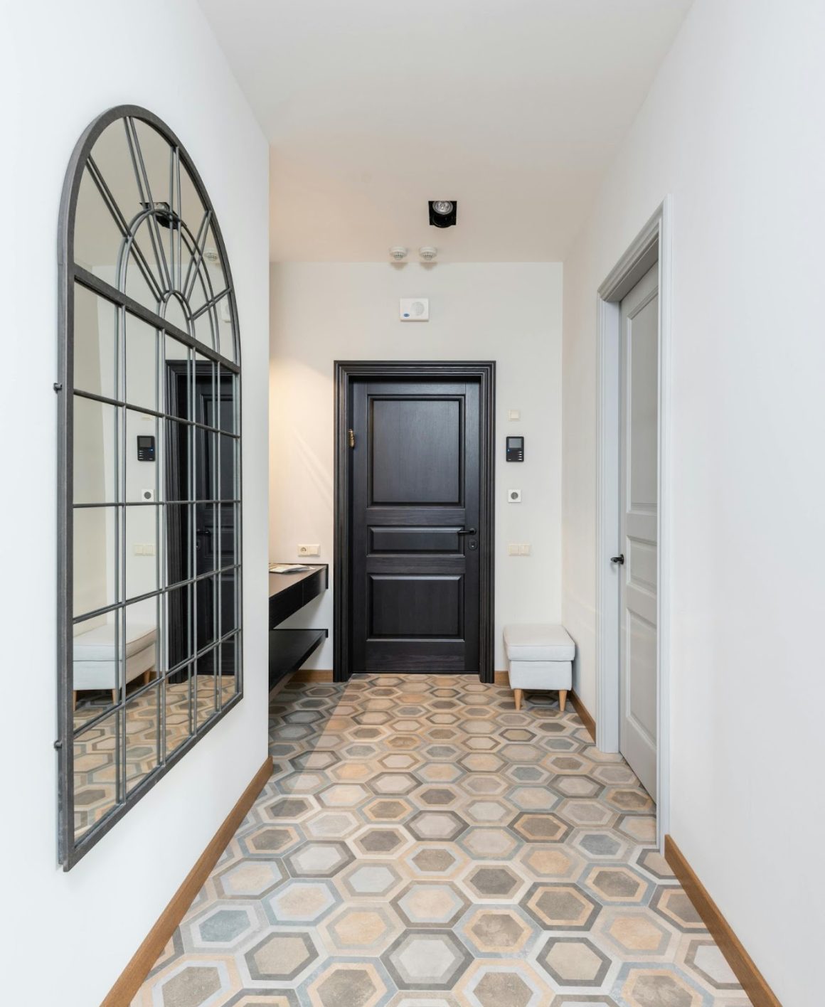 Un couloir carrelé hexagonal avec un motif en noir et blanc et une porte en bois au fond.