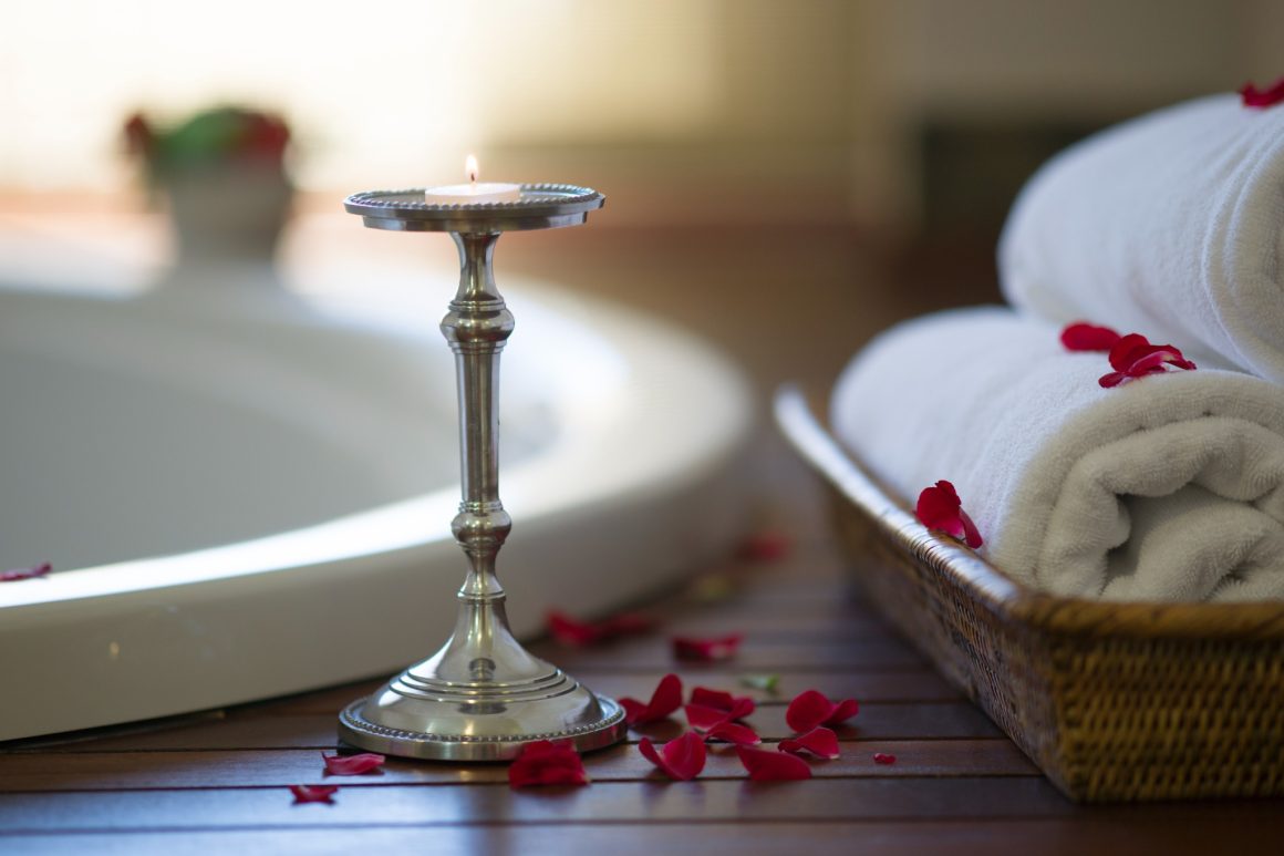 une salle de bains avec une bougie sur un chandelier argenté, des serviettes blanches et des pétales de rose rouge