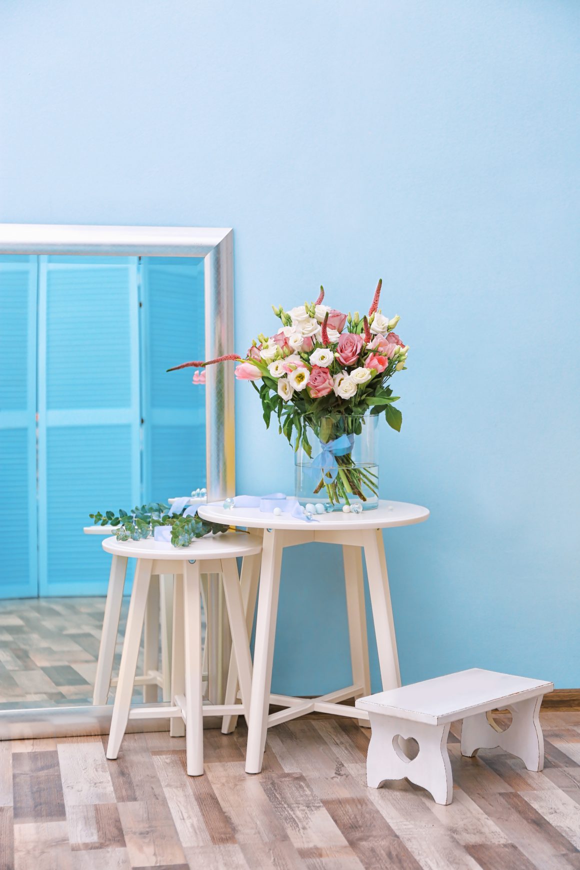 Un mur de véranda peint en bleu clair, avec une table blanche, un bouquet de fleurs colorées et un miroir