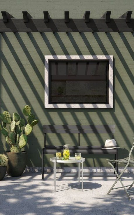 Un mur de véranda peint en vert olive, avec des plantes en pot et des meubles de jardin en métal