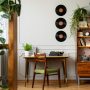 Un bureau en bois avec une chaise assortie est décoré de plantes en pot. Des disques vinyles sont accrochés au mur complétant cette déco rétro