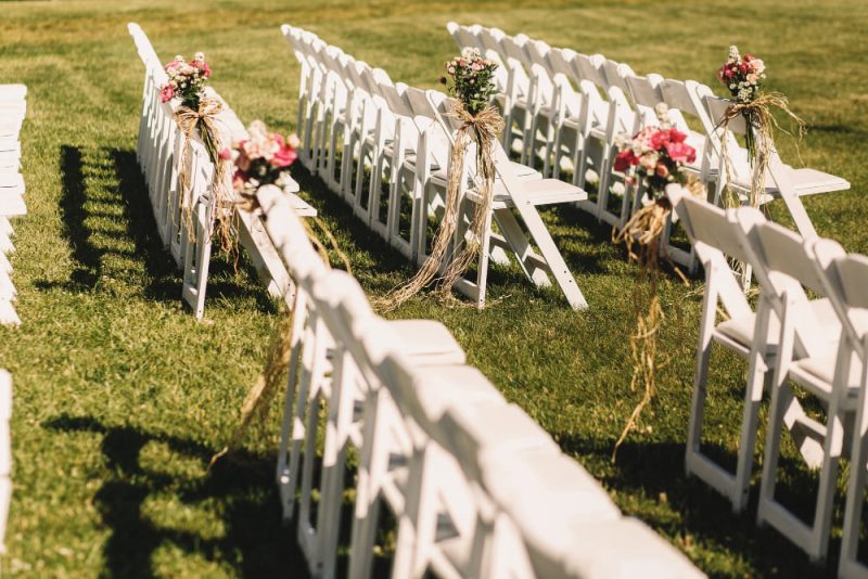 Une décoration mariage extérieur avec des chaises blanches des deux côtés de l'allée nuptiale
