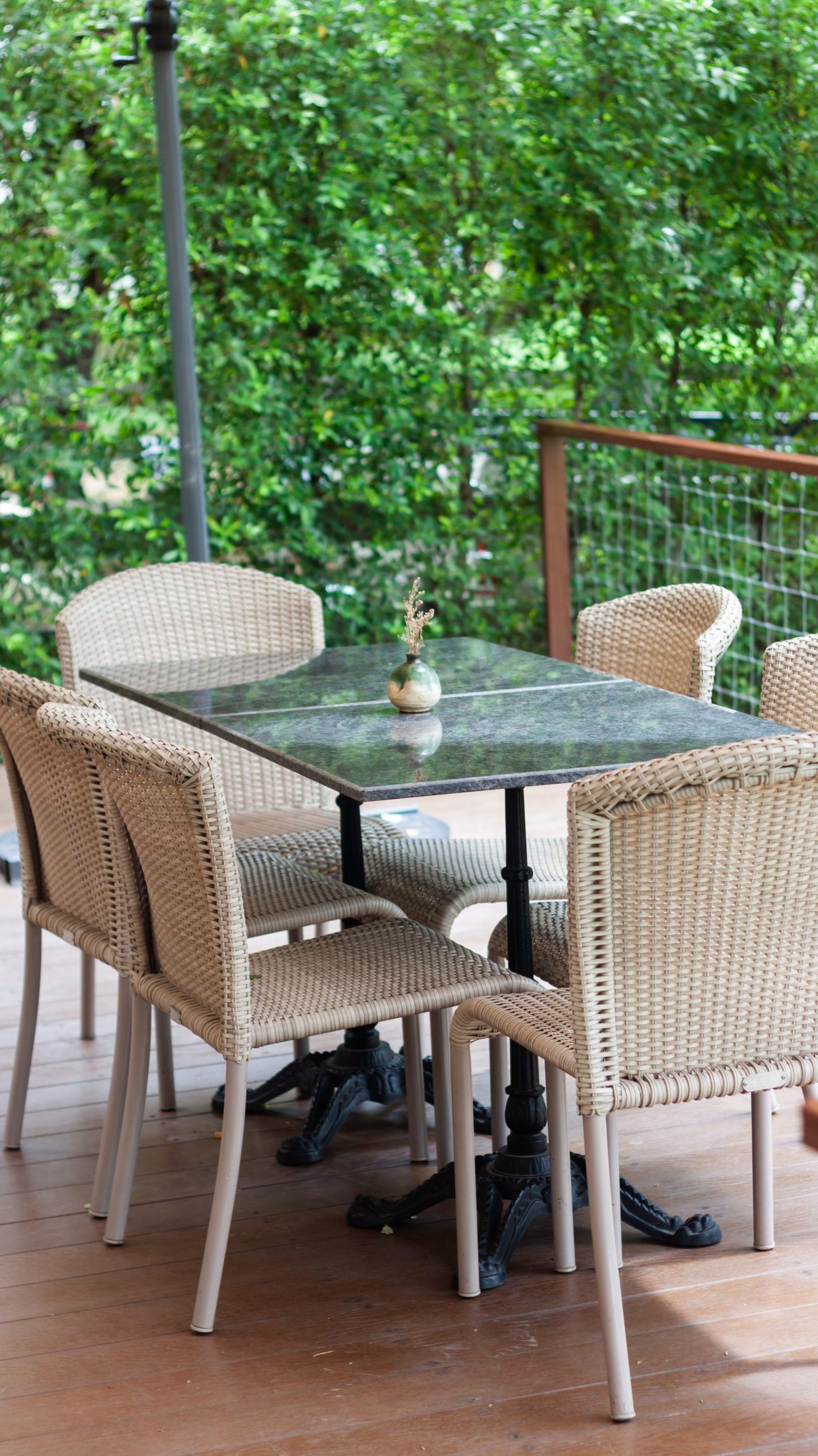 espace de coin repas extérieur avec table en verre et chaises en osier sur une terrasse en bois, entouré de feuillage vert