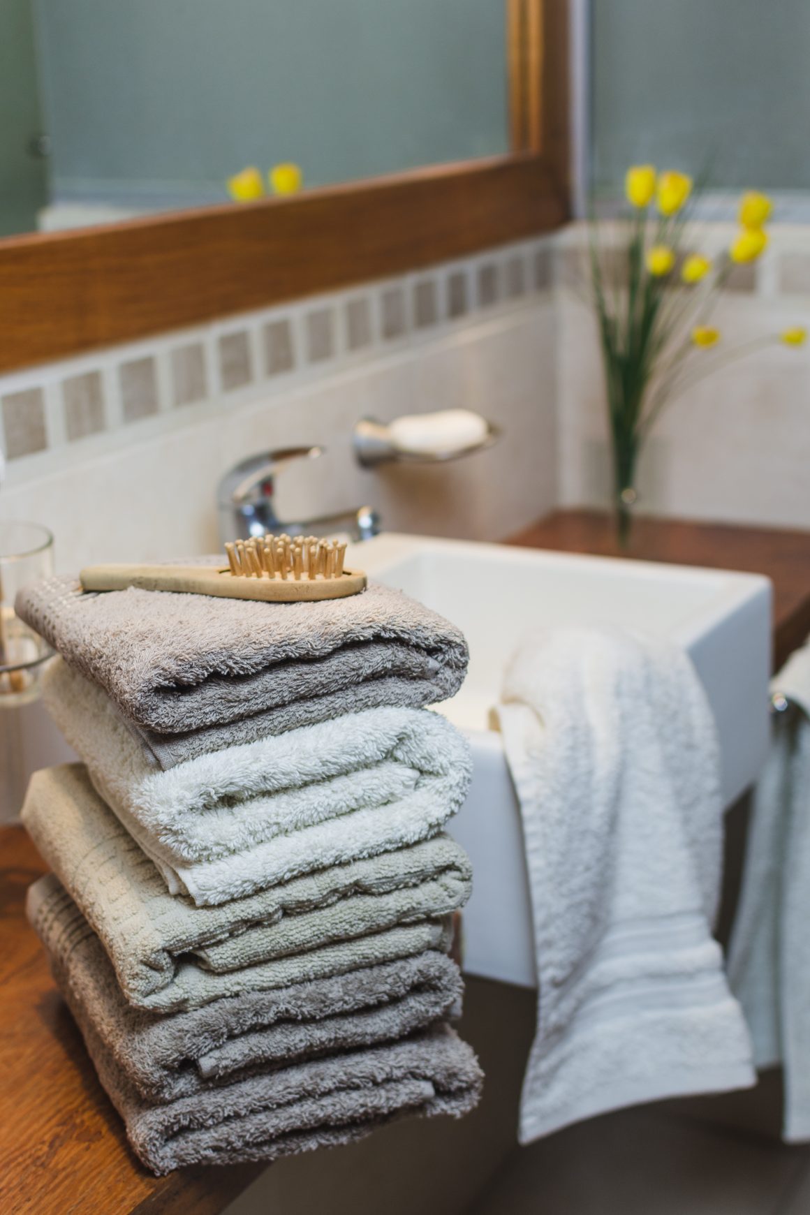 une salle de bains avec des serviettes beige et une brosse sur le lavabo, avec des fleurs jaunes en arrière-plan