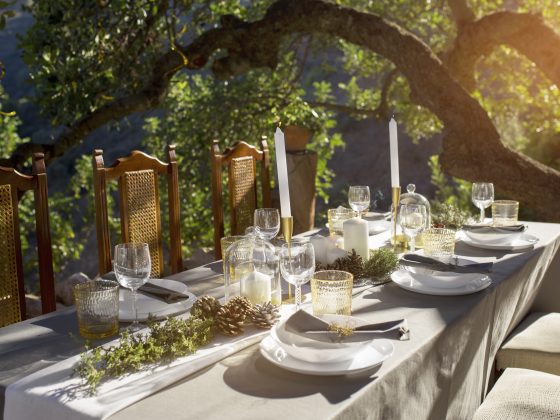 une table élégante dressée pour un repas en plein air sous un arbre, avec des assiettes blanches, des verres et des bougies