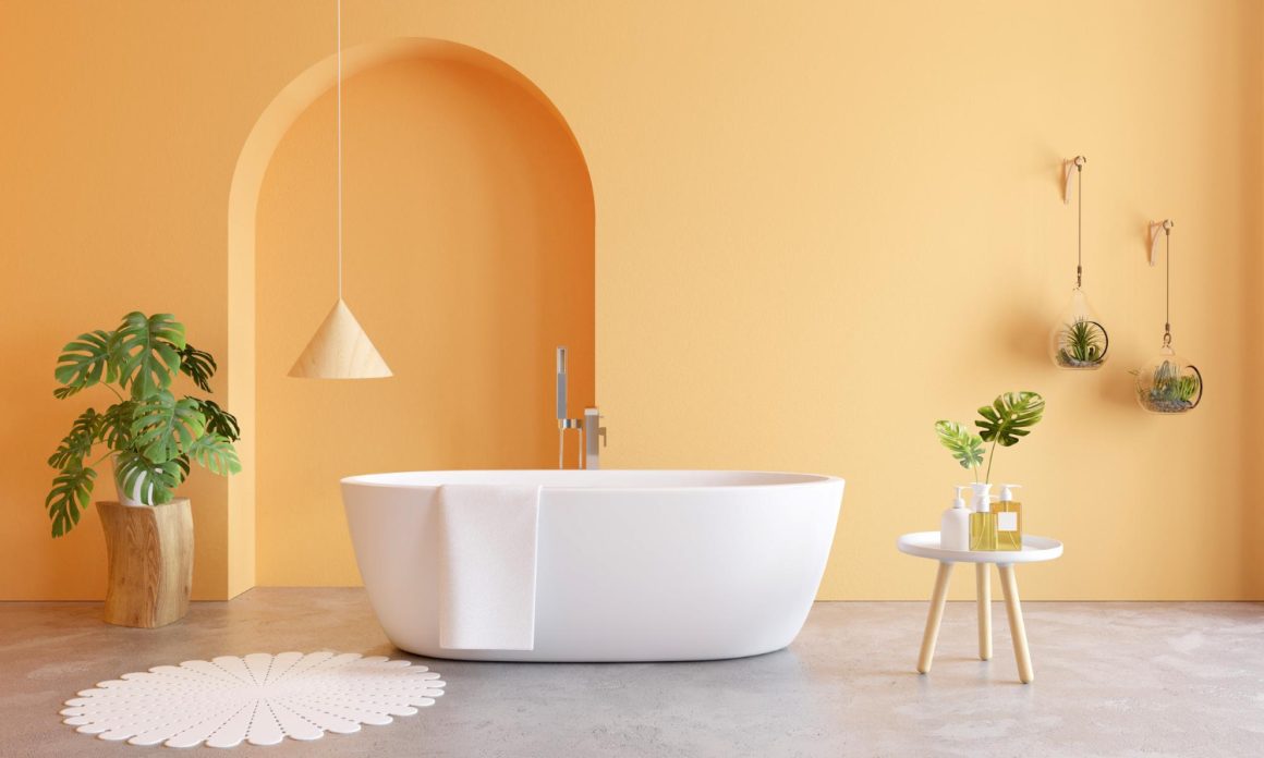 Espace lumineux présentant des couleurs tendance salle de bain avec des murs orange doux, une baignoire blanche, des plantes vertes luxuriantes, un tapis blanc à motifs et des accents en bois naturel.