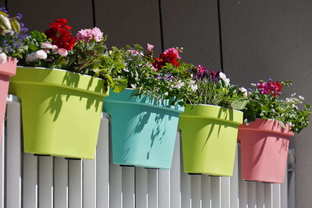 une décoration balcon étroit avec quatre pots de fleurs colorés en plastique, installés sur la rambarde