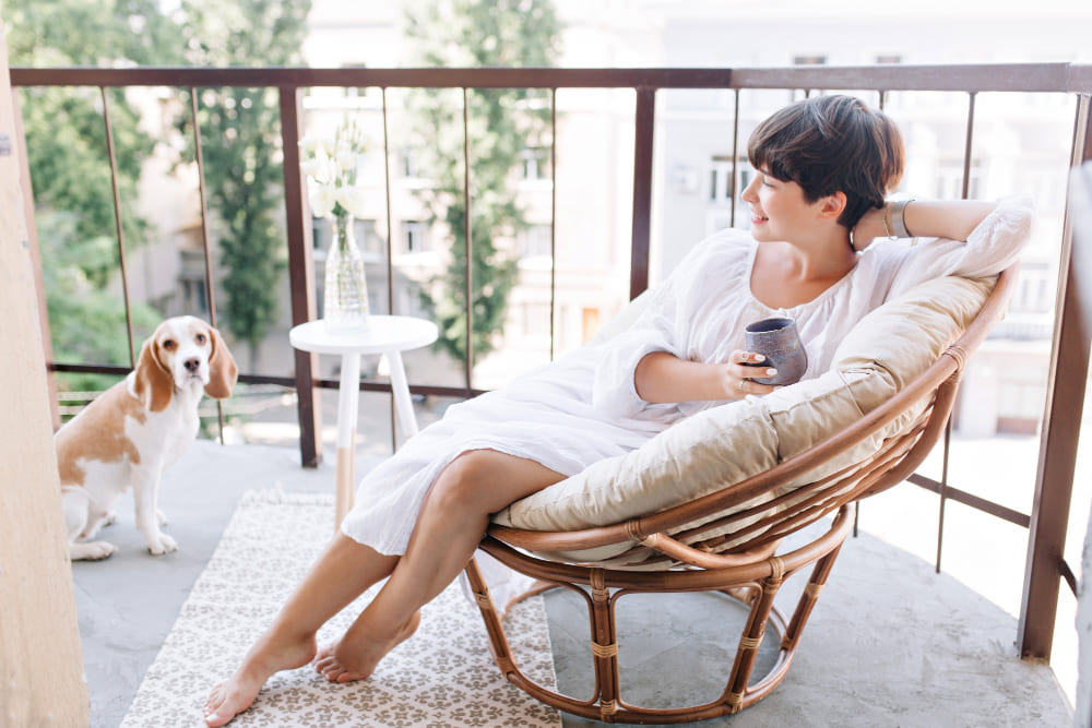 une femme dans un fauteuil en osier, sur la terrasse, avec un chien à côté