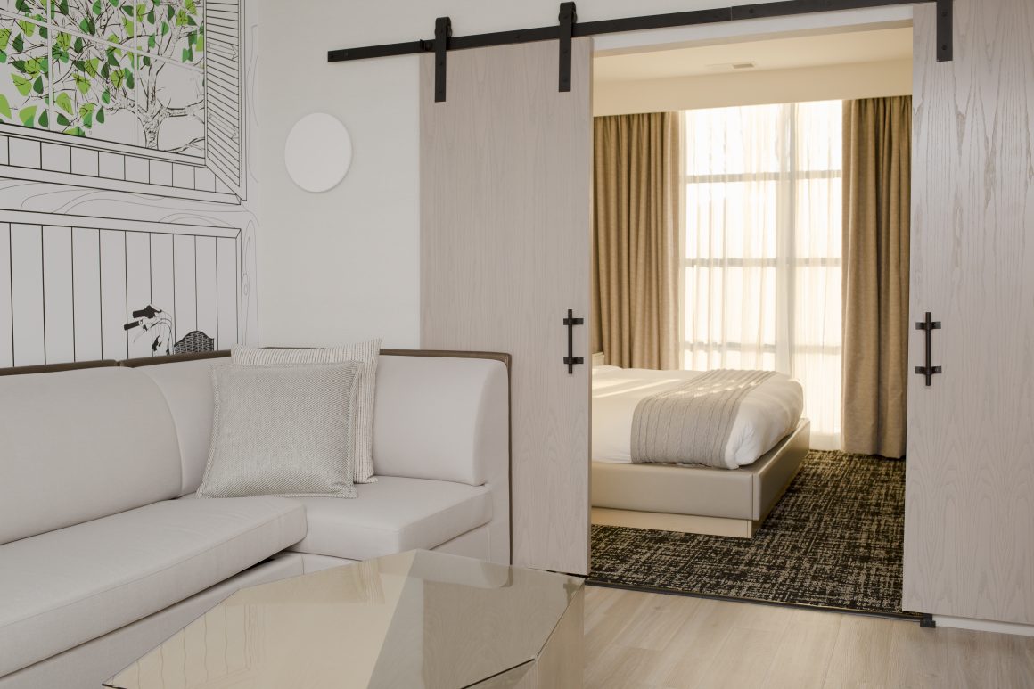 Un salon moderne et lumineux, avec un canapé confortable, une table en verre, et une chambre séparée par des portes coulissantes élégantes.