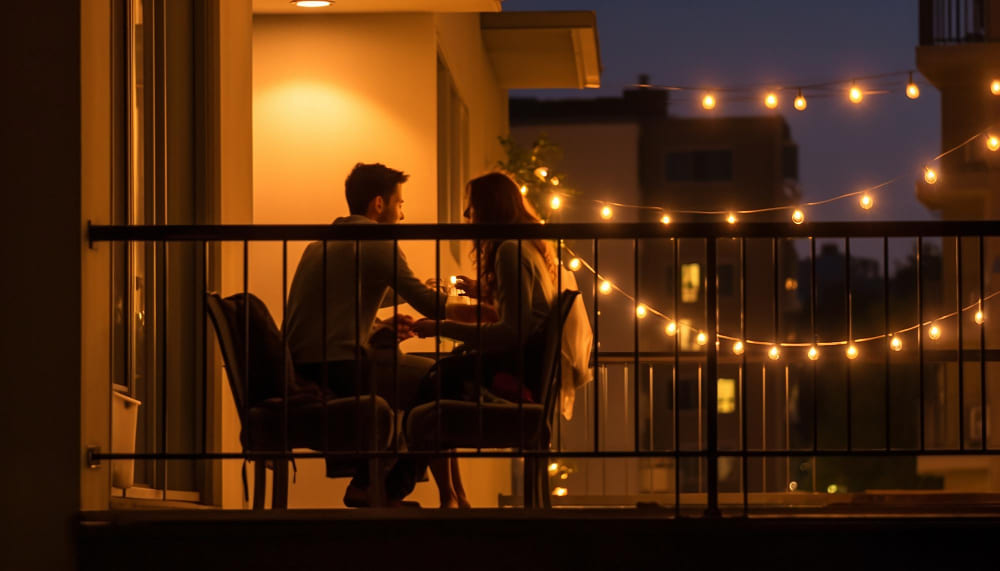 un couple d'amoureux dîne sur sa petite terrasse, décorée avec des guirlandes lumineuses