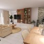 espace de vie aménagé par un architecte rénovation chez pipcke, comprenant une salle à manger et un salon qui inclut un canapé beige, une table ronde en bois, un meuble TV en blanc et bois, des étagères décoratives, des rideaux légers, des plantes vertes et un tapis en jute.