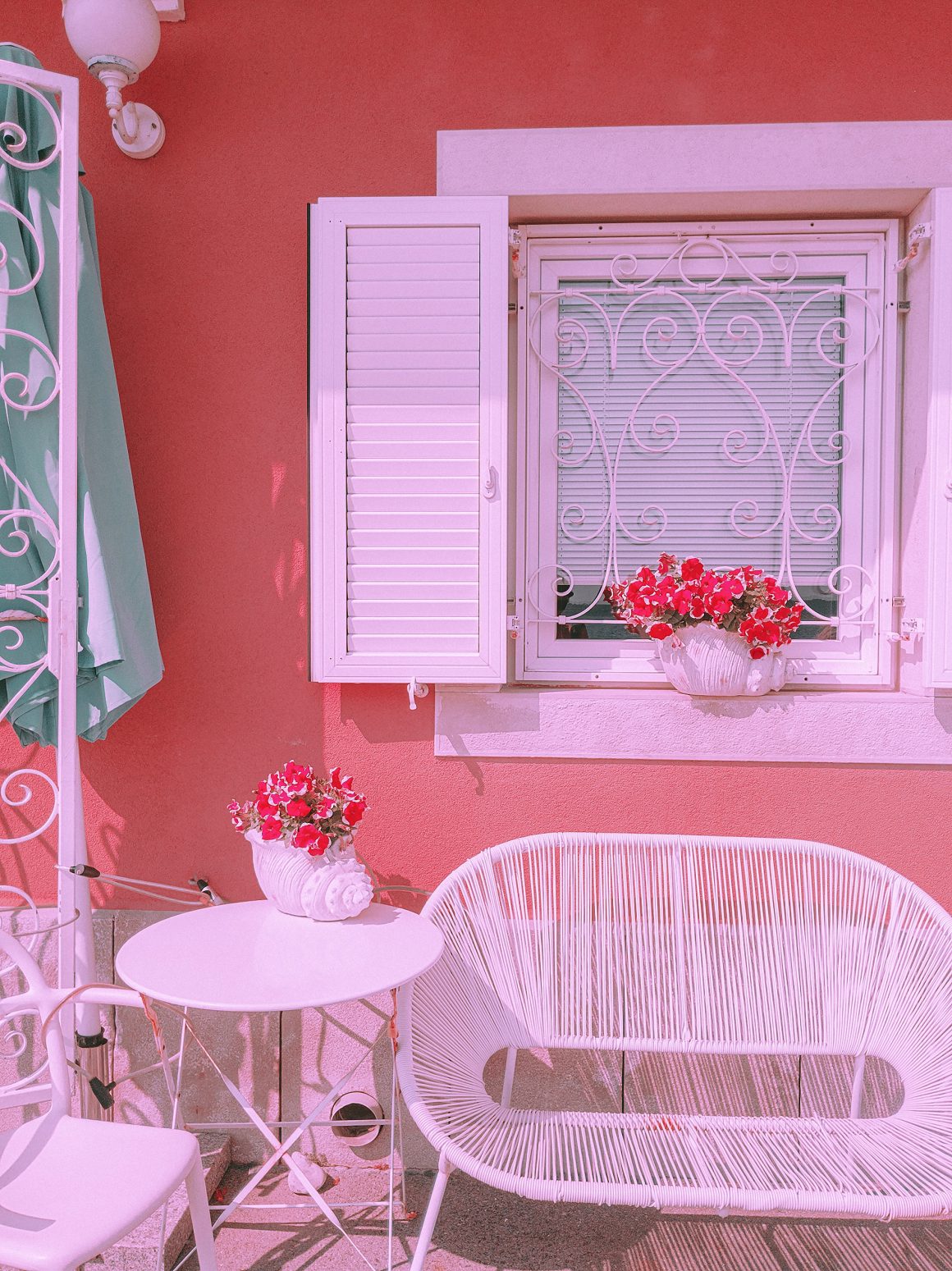 aménager un petit balcon charmant avec des murs roses, des pots avec des fleurs rouges et un mobilier blanc.