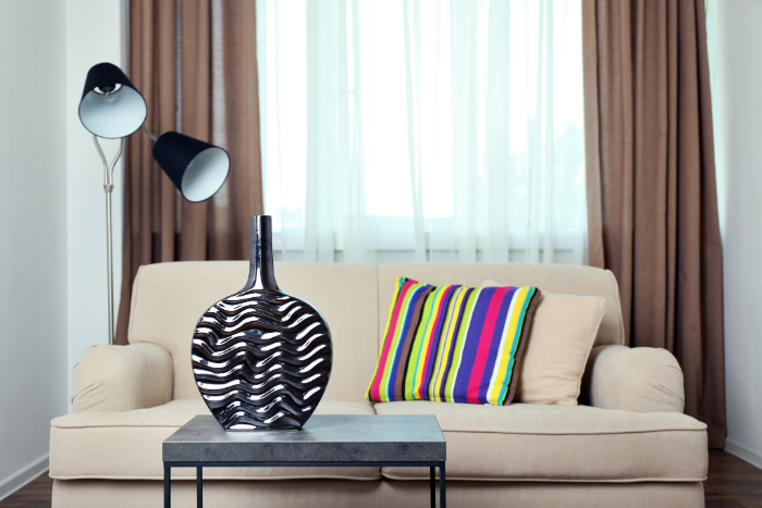 canapé 2 places beige, un coussin coloré, une lampe et un vase design.