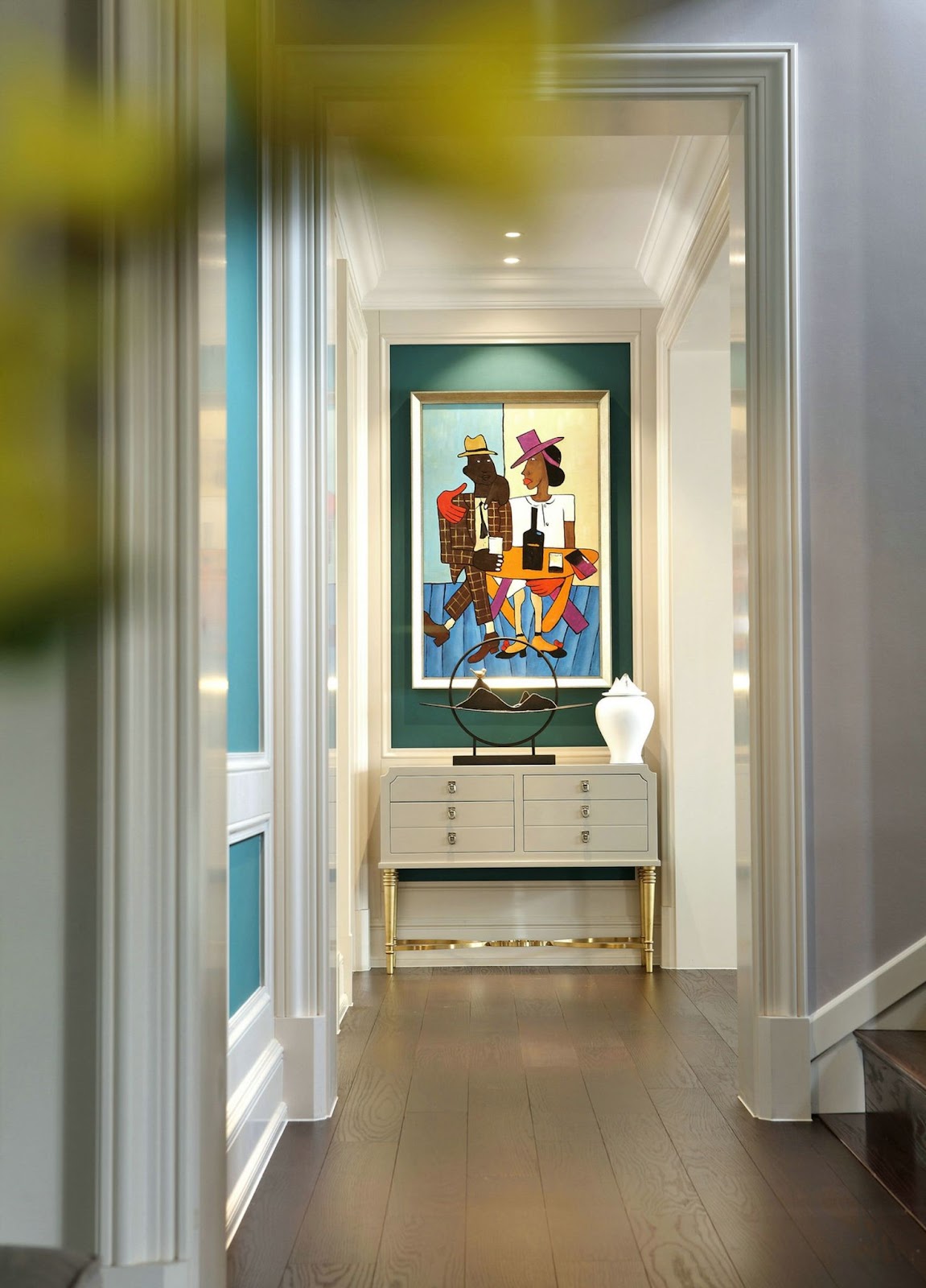 Couloir avec moulures blanches, murs bleu profond et une console chic, sublimé par un tableau coloré.