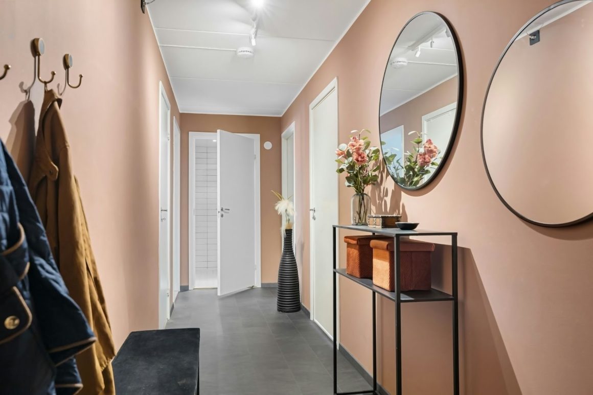 Couloir moderne aux murs beige rosé, décoré de miroirs ronds, d’une console élégante et de touches florales.