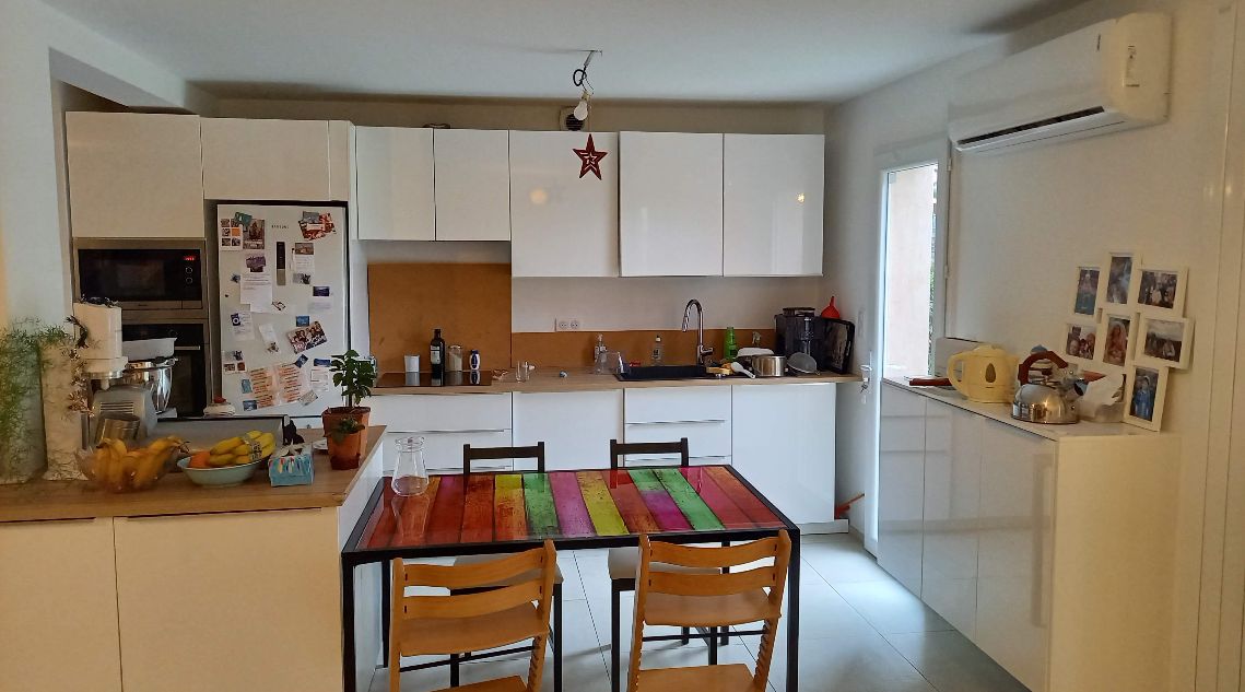 une cuisine dans son jus, avec des meubles en bois blanc et une crédence en bois naturel, avec une table colorée