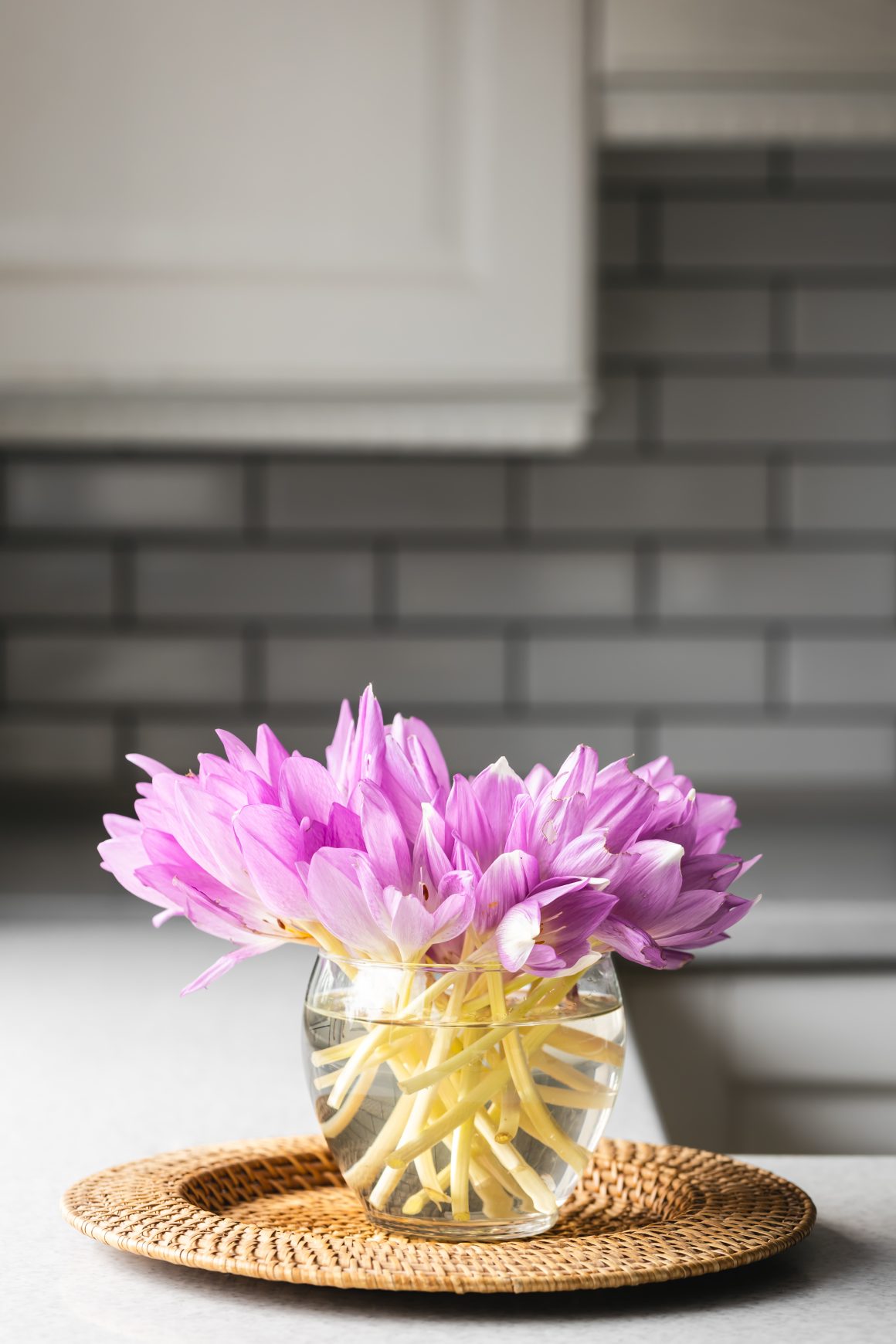 Fleurs roses dans un vase transparent, sur plateau en osier.