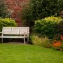 une décoration jardin extérieur avec un banc sur la pelouse verte, au milieu des buissons et des fleurs