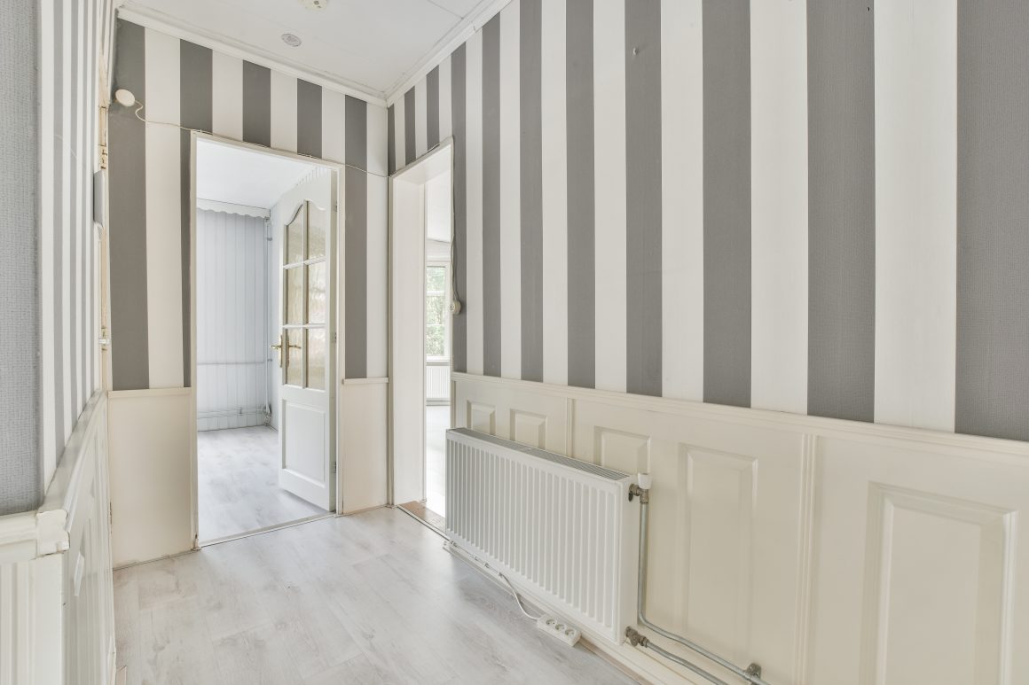 Peinture couloir étroit avec des murs rayés gris et blanc et un sol en bois clair.