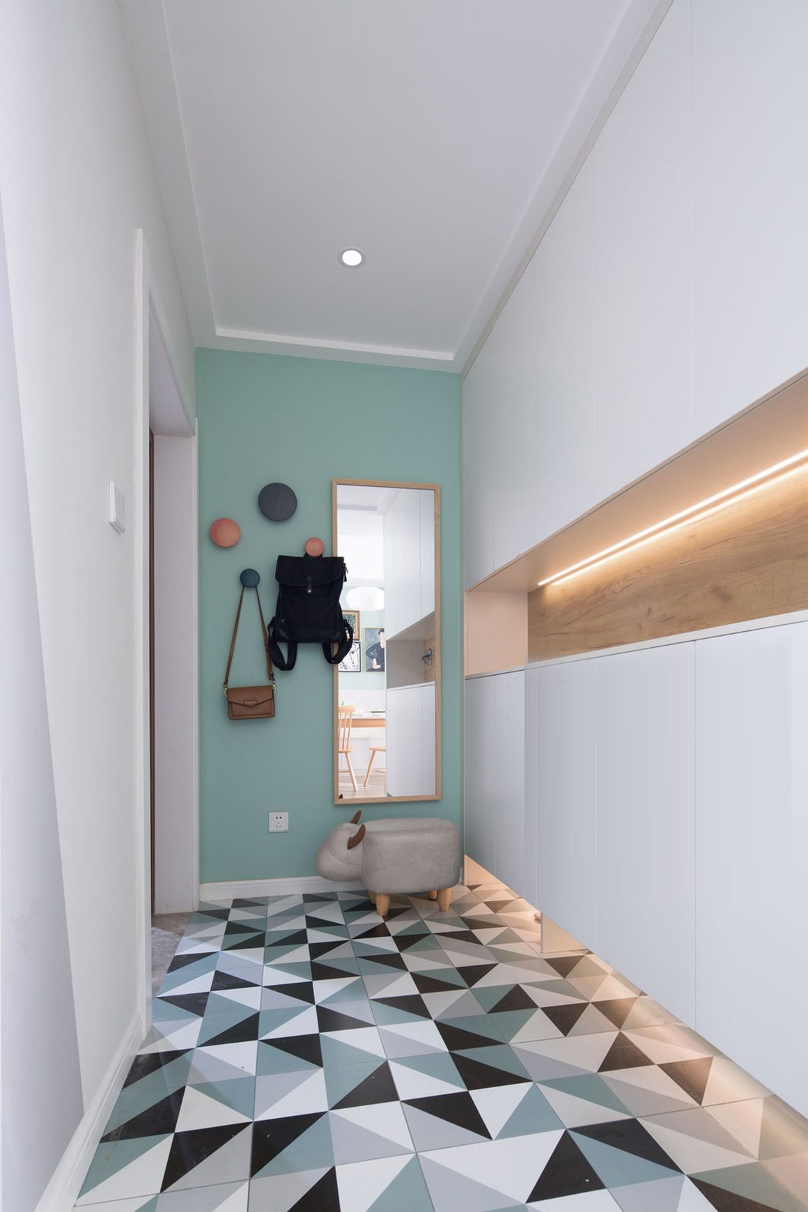 couloir moderne avec des murs blancs, miroir, rangement intégré et carrelage géométrique coloré.