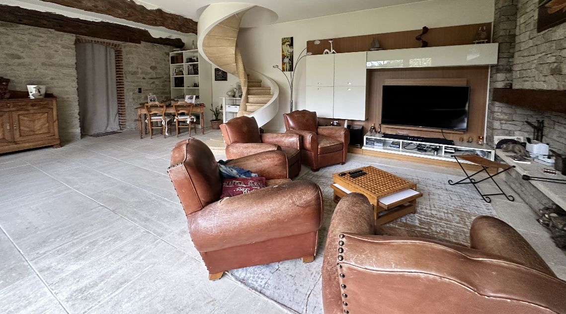 Un salon spacieux avec des fauteuils en cuir, une table basse, une télévision, une bibliothèque et un escalier en colimaçon.