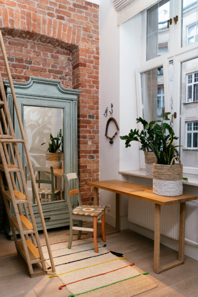 Intérieur chaleureux avec mur en brique, meubles en bois, plantes, échelle, et tapis coloré.