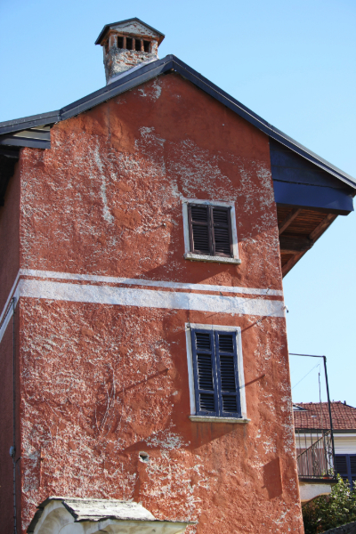 Maison ancienne à l'enduit rouge décrépi, avec fenêtres à volets et toit en pente.