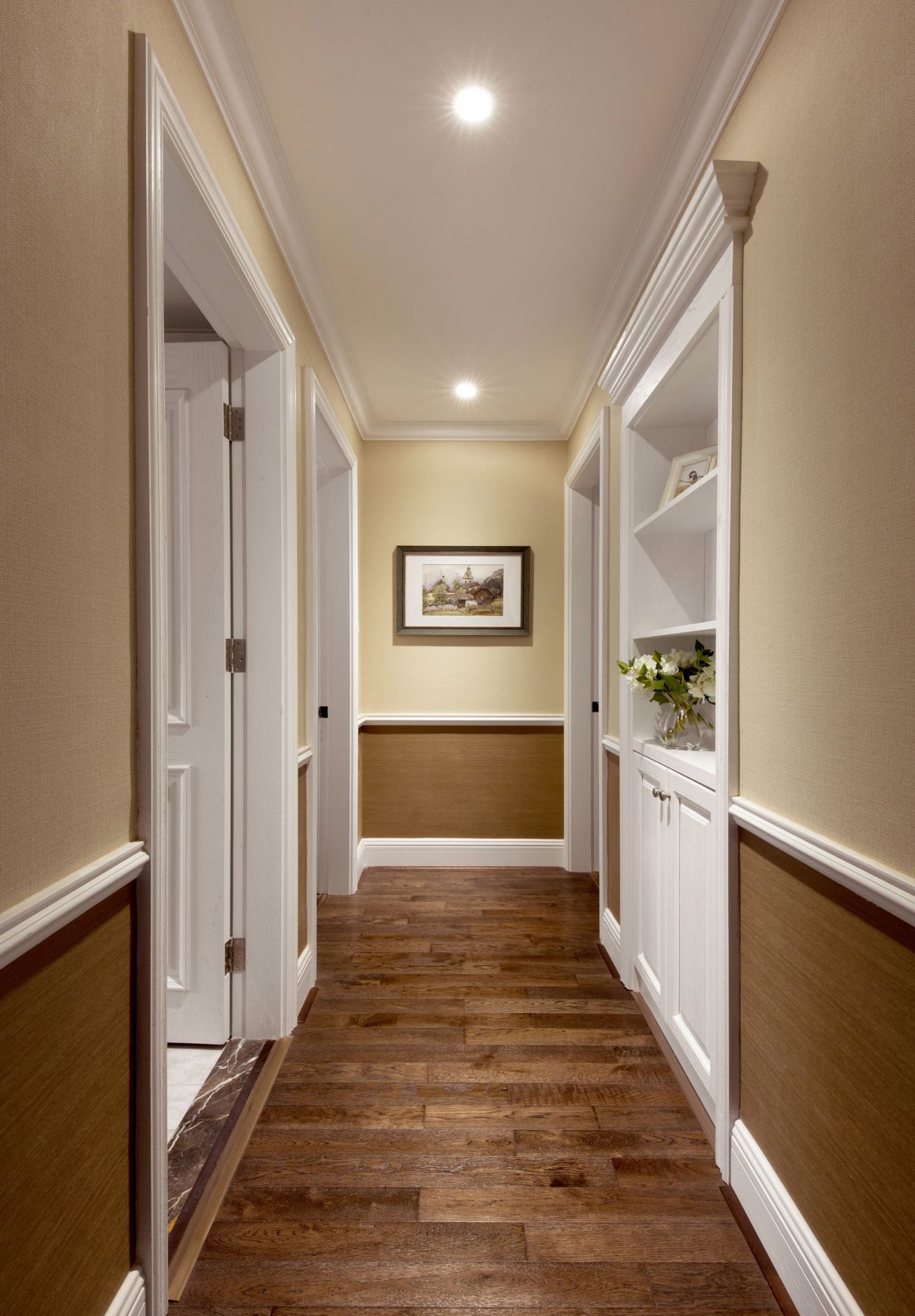 Un couloir lumineux avec des murs beige, plancher en bois, étagères blanches et cadre décoratif.