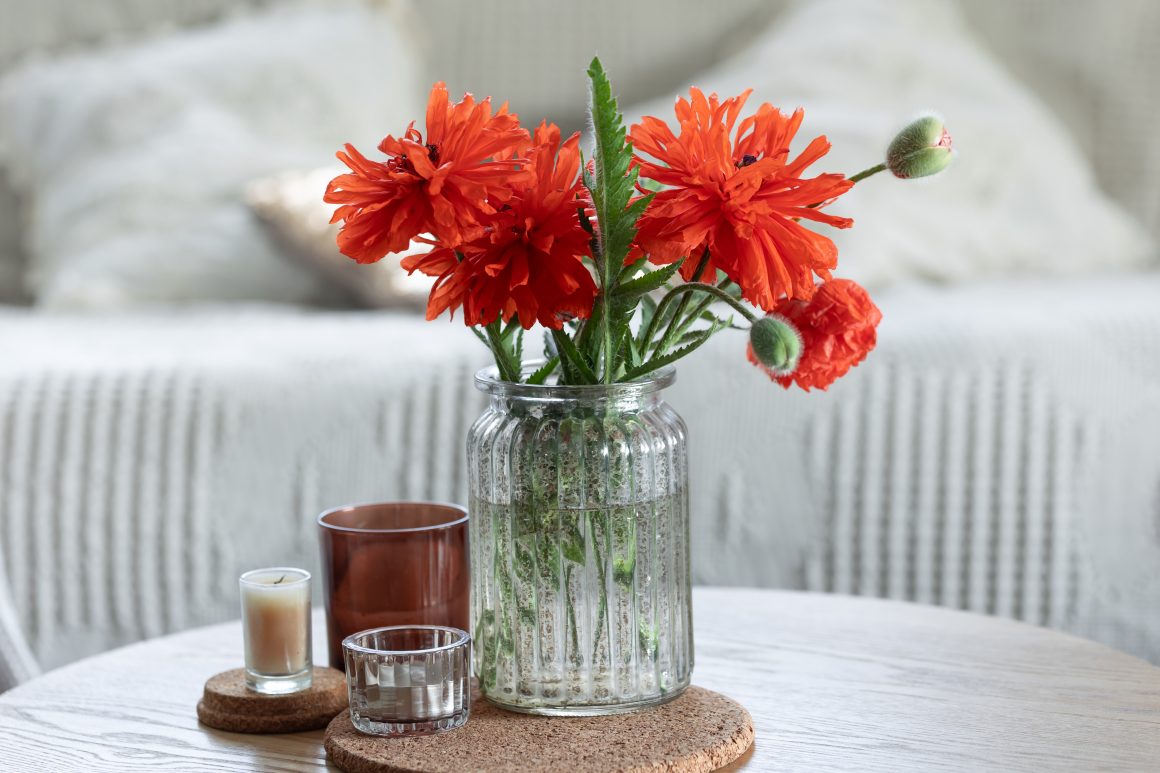 Un vase en verre contient des fleurs orange, accompagné de bougies sur une table en bois.