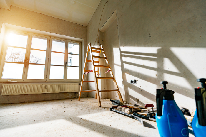 Une pièce en rénovation avec une échelle, des outils, des lumières naturelles et murs nus.