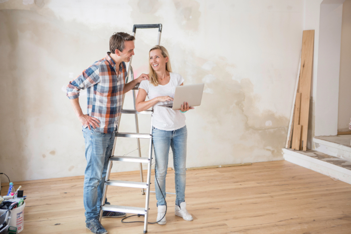 Couple souriant sur une échelle, travaillant sur rénovation ensemble.