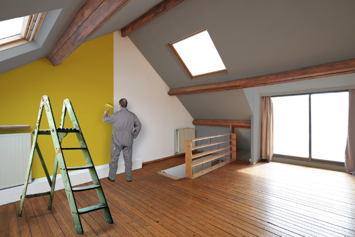 Un homme effectue des travaux de rénovation dans une maison ancienne en peignant un mur jaune.