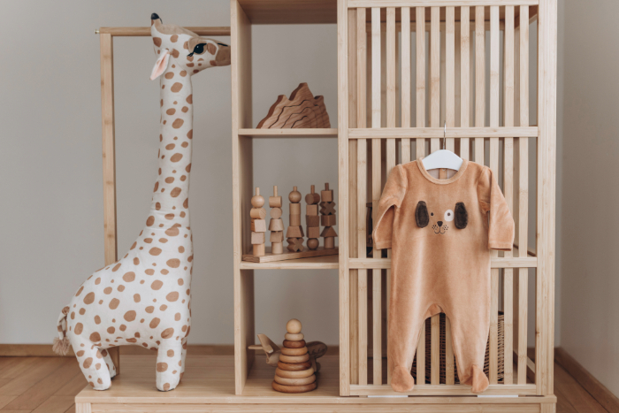 Chambre bébé style jungle avec grande girafe en peluche et une armoire en bois clair au design épuré, incluant vêtements bébé suspendus et des jouets en bois.