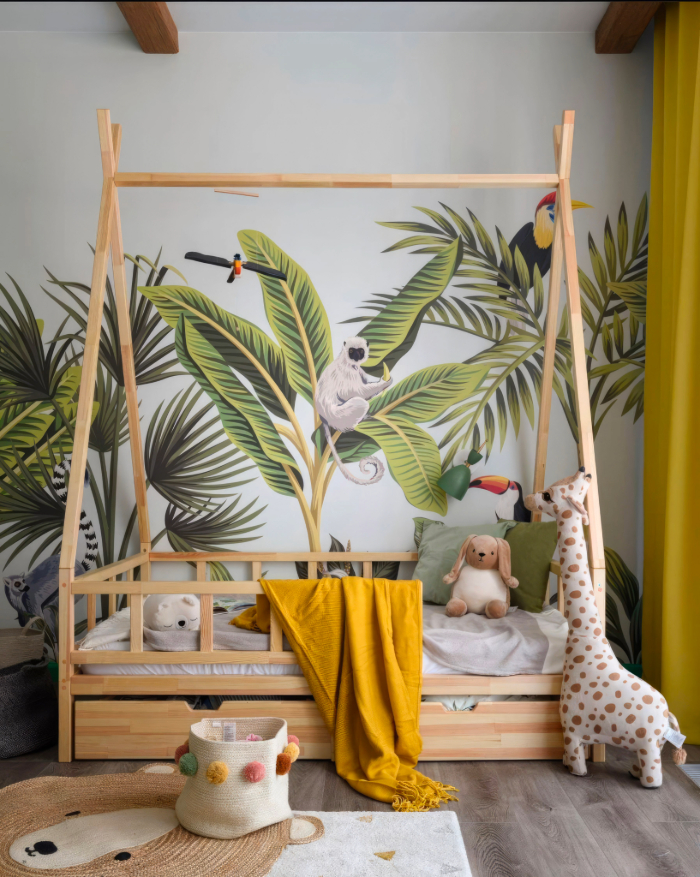 Chambre bébé jungle avec lit en bois, mur jungle peint, peluches, couverture jaune, rideaux verts, tapis rond et décor ludique.