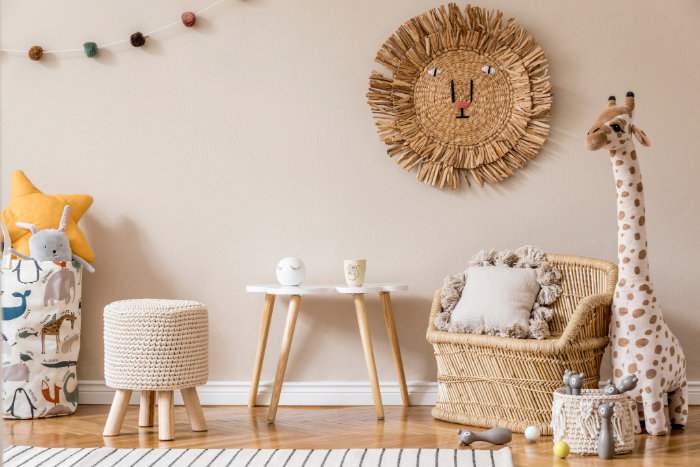 Chambre bébé thème jungle incluant un fauteuil en osier, grande girafe en peluche, tapis rayé, table blanche, pouf tricoté et des jouets doux.